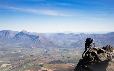 A photographer climbing a steep and exposed ridge while on a hike in the mountains.