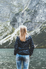 A young blonde girl looks at the spring lake and mountains