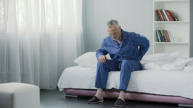 Retired man sitting in bed and feeling terrible pain in back, health and illness