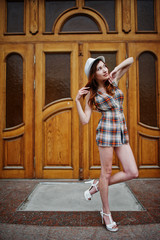 Obraz na płótnie Canvas Amazing long legs with hig heels girl wear on hat posing against large wooden doors.