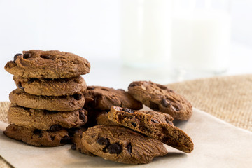 Chocolate chip cookies on brown paper and sack cloth with glass of milk on white background. With copy space for text.