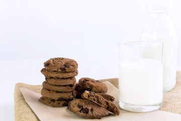 Chocolate chip cookies on brown paper and sack cloth with glass of milk on white background. With copy space for text.