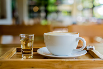 Hot cappuccino coffee and syrup on wooden tray with burred and bokeh background