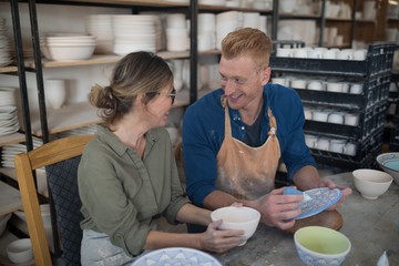 Male and female potter interacting while decorating earthenware
