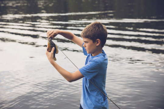 Side View Of Boy Removing Fish From Fishing Rod At Lake