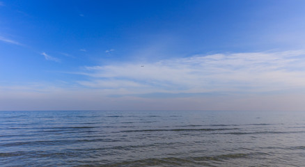 Calm sea and blue sky with white clouds background. An airplane fly on the horizon.