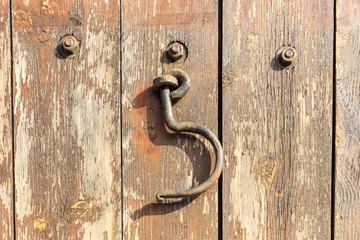 Rusty hook hanging on an wooden door. Close up view.