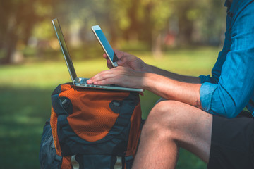Man with a backpack sitting in a park and holding a phone in his hand. Digital nomad concept