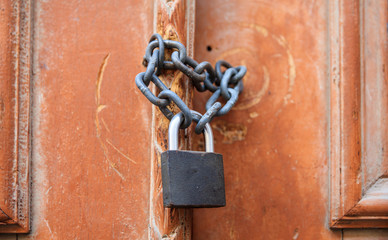 Padlock with chain blocking the entrance. Wooden door, close up view.