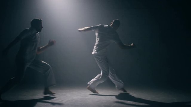 Two men practicing capoeira in dark room