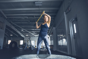 Woman hitting tire with sledgehammer while training at gym
