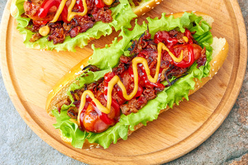 Two homemade hot dogs with lettuce, bacon and onion toppings 
