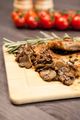 Close up image on pork steak on wooden board next to grilled mushrooms and cherry tomatoes