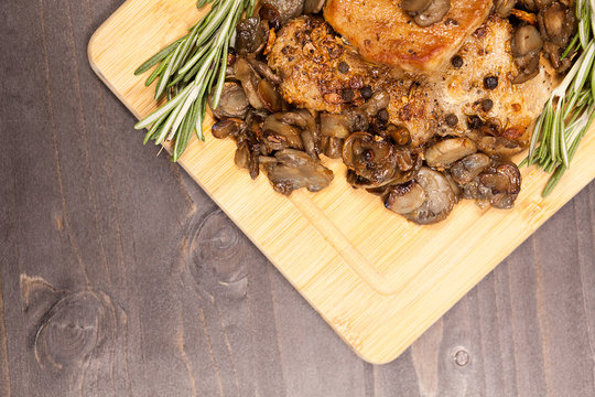Over top view on pork steak with grilled mushrooms next to a brunch of oregano on wooden board