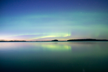 Northern lights dancing over calm lake in Farnebofjarden national park in Sweden