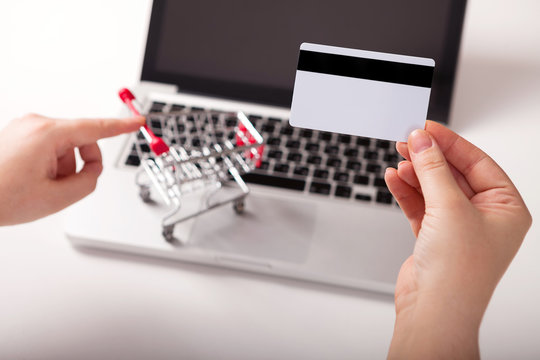  Bank card nearby a laptop and mini shopping cart on white background top view.