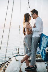 A stylish couple in love stands on a yacht on which she spends their honeymoon, they hugs and kiss each other