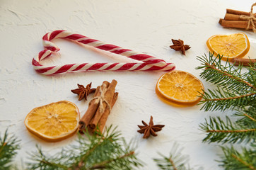 Heart of candy cones on the white table with traditional spices anise stars, cinnamon sticks, dried oranges. New year food decorations with fir branches. Christmas composition greeting card. Side view