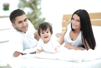 Happy young family with a baby lying in bed and smiling