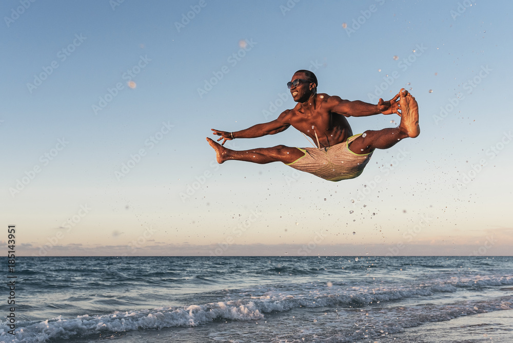 Wall mural young man jumping into the beach.