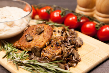 Close up on grilled pork steak, mushrooms cherry tomatoes and a plate with bean paste on wooden plate on a table