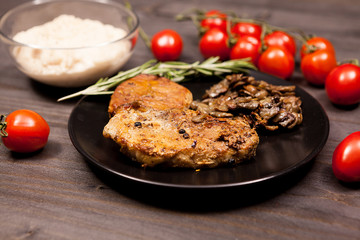 Pork steak in black plate with grilled mushrooms, oregano cherry tomatoes and bean paste on a wooden table