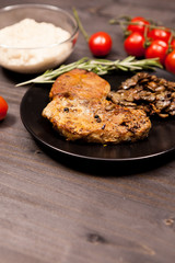 Pork steak in black plate with grilled mushrooms, oregano cherry tomatoes and bean paste on a wooden table