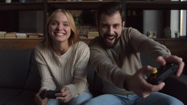 Cheerful day. Delighted couple sitting on the sofa while using joypads and playing video games