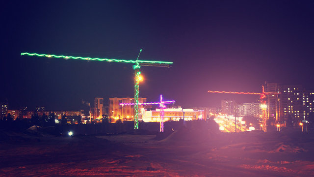 Construction cranes at a construction site, colored light at night, lights and LEDs