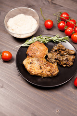 Grilled pork steak in black plate with grilled mushrooms, oregano cherry tomatoes and bean paste on a wooden table
