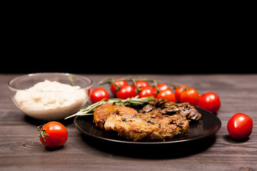 Delicious Pork steak in black plate with grilled mushrooms, oregano cherry tomatoes and bean paste on a wooden table