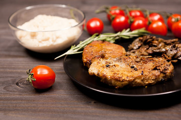 Roasted Pork steak in black plate with grilled mushrooms, oregano cherry tomatoes and bean paste on a wooden table