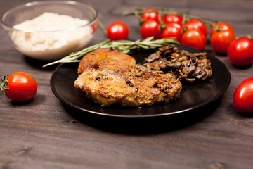 Roasted pork in black plate with grilled mushrooms, oregano cherry tomatoes and bean paste on a wooden table