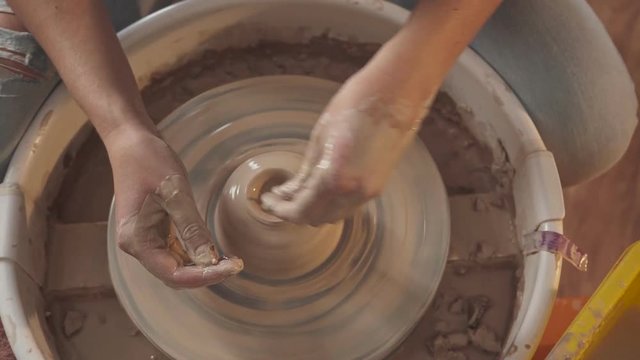 Hands in clay carefully and gently touch the figure on the potter's wheel. Work of the potter: fine craftsmanship and creation of stylish objects. Potter's hands work with clay on a potter's wheel.