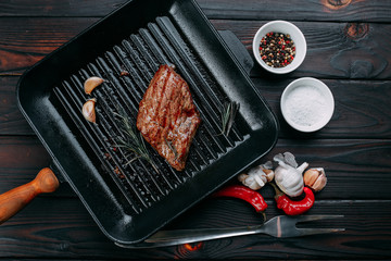 Beef steak with rosemary, chili pepper, garlic and spices on the grill pan, flat lay. Restaurant kitchen, cooking concept