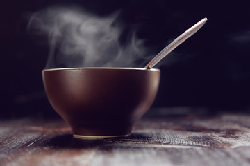 brown steaming bowl of hot meal with spoon on wooden table close up