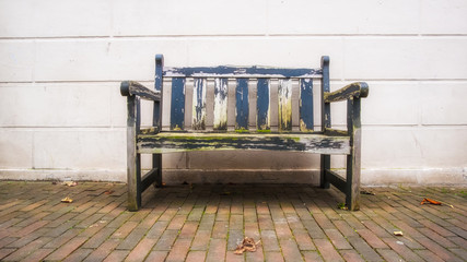 Used old Bench in front of white wood wall standing on cobblestone in urban area