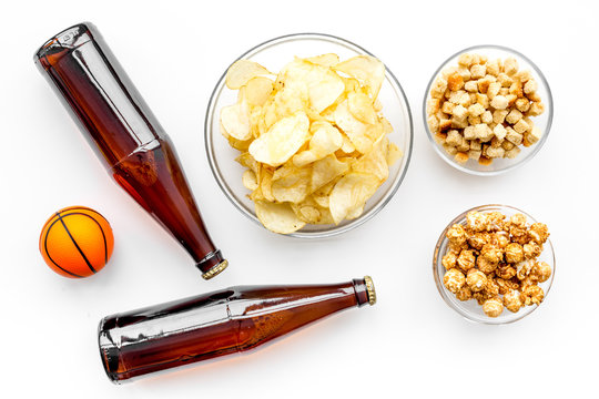 Snacks for watching sport matches and games on TV. Crisps, popcorn, rusks near drink and ball on white background top view