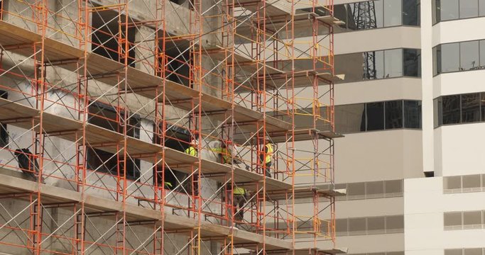 A long shot of construction workers on scaffolding on the side of a building in a large city.  	