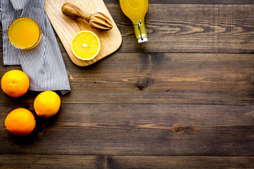 Healthy vitamin drink. Fresh orange juice near fruits and juicer on dark wooden background top view...