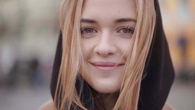 Closeup portrait of female lovely face with green eyes and clean skin smiling joyfully while wind blowing her light brown hair in slow motion. Movie style