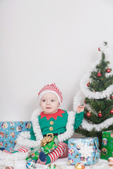 Boy in Christmas Elf costume. A baby near a Christmas tree.