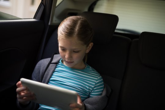 Teenage girl using digital tablet in the back seat