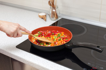 Vegetables are in a frying pan. Woman cooking colourful fresh vegetables on an electric stove