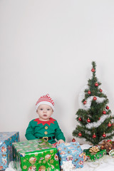 Boy in Christmas Elf costume. A baby near a Christmas tree.