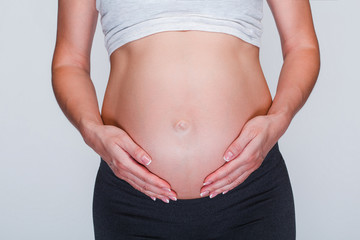 Mother protection. Part of young pregnant woman touching her belly while standing at white background