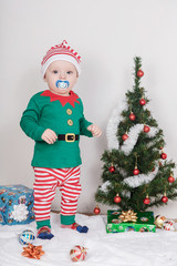Boy in Christmas Elf costume. A baby near a Christmas tree.