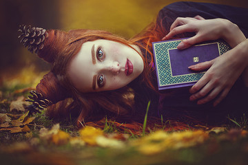 Portrait of a beautiful red-haired girl with an unusual hairdo with a book in the autumn fairy...