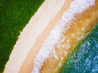 Aerial view of the tropical beach with clear water with waves and green grass meadow