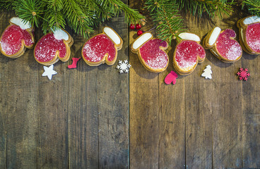 christmas mittens shaped cookies and fir branches on dark rustic wooden background with copy space